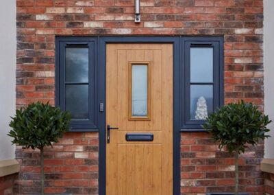 Malvern composite door in light oak with grey outerframe and heritage hardware.